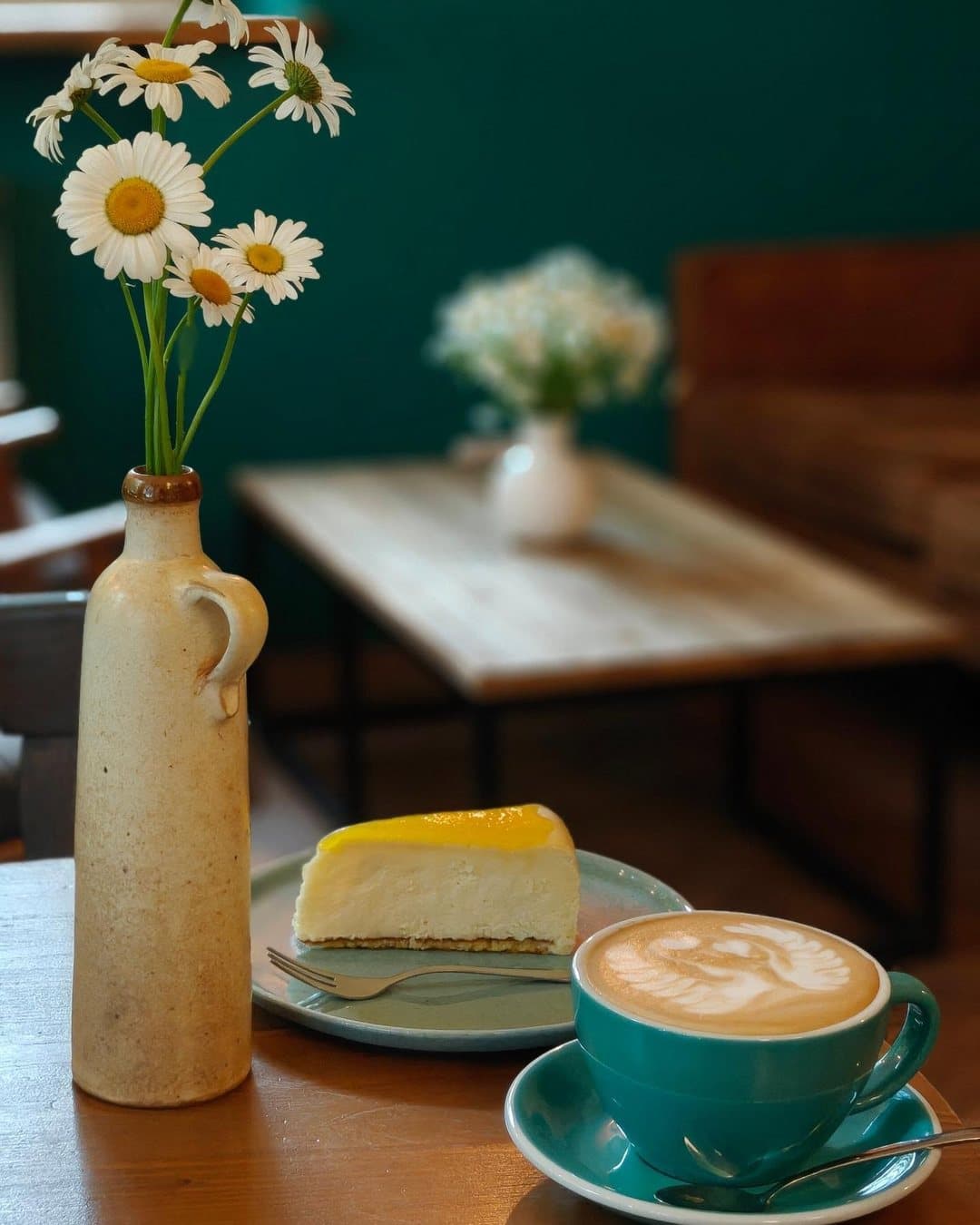 Cappuccino, sūrio pyragas ir ramunės ant staliuko